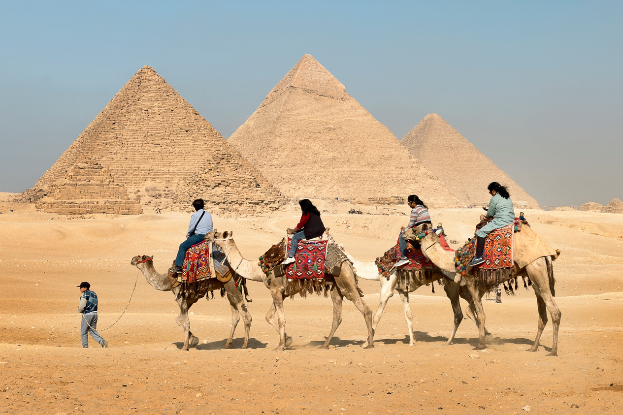 Four People Riding on Camels Across the Pyramids